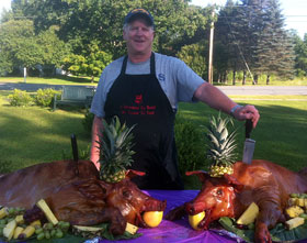 Terence Lernihan poses with two "fully dressed" pig and fruit platter displays - pineapple hat, apple in mouth, against a bed of fruits and greens.